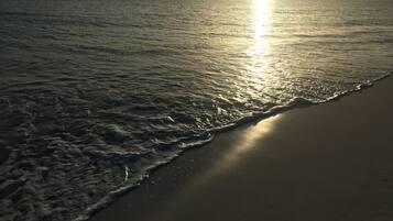 A beach with waves gently lapping onto the shore and the sun setting in the background.