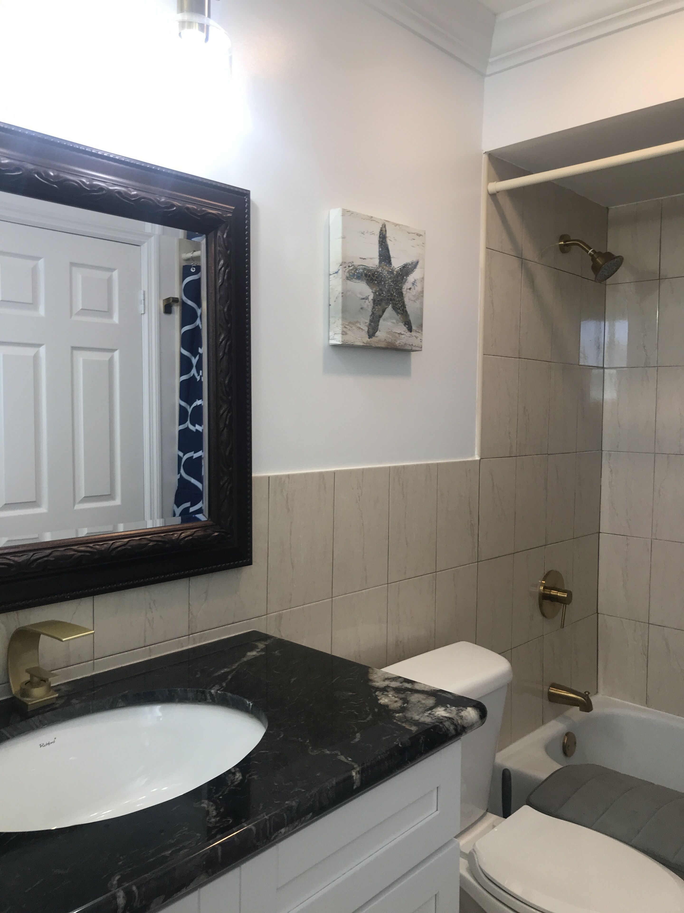 A bathroom with a white sink, a large mirror, a starfish artwork, a shower with a handheld showerhead, and a toilet.