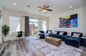 A spacious living room with a large blue sofa set, a wooden coffee table, and a ceiling fan.
