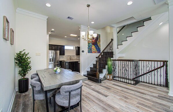A spacious dining area with a wooden table and chairs, a chandelier, and a staircase with a metal railing.