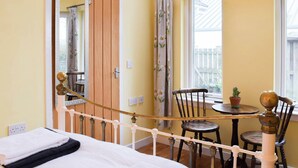 Ein Schlafzimmer mit einem Bett, einer Holztür, einem Fenster mit Vorhängen, einem kleinen Tisch mit Stühlen und einer Topfpflanze.