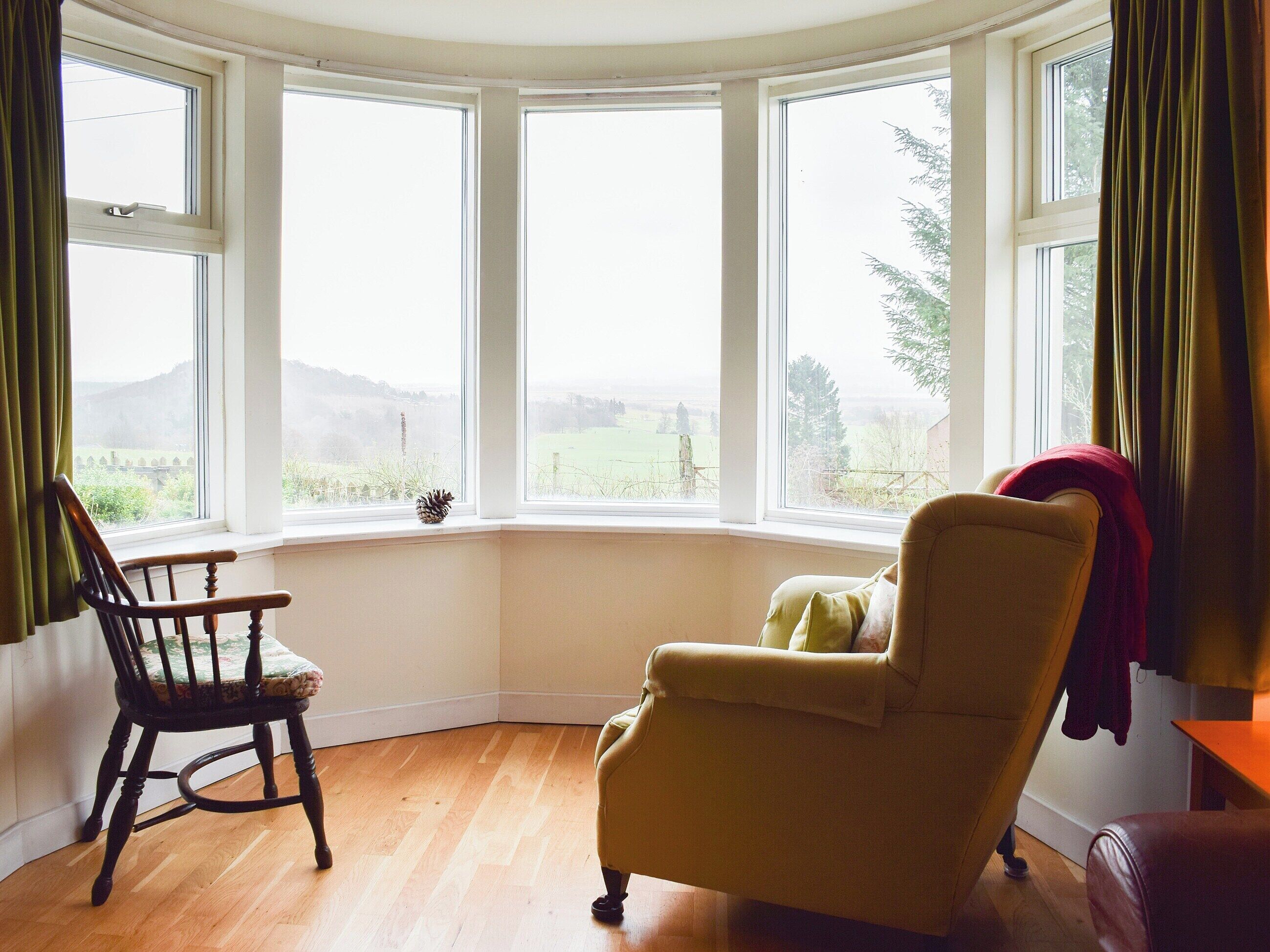 Una habitación con ventanal panorámico, una silla de madera, un sofá y vistas a un paisaje verde.
