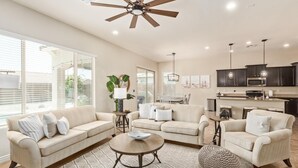 A spacious living room with a large ceiling fan, a dining area with a table and chairs, and a kitchen with dark cabinets and stainless steel appliances. - Three Palms at Estrella Mtn Ranch - 3BD with Private heated pool & spa (Goodyear)
