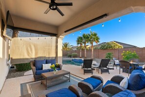 An outdoor patio with a ceiling fan, wicker furniture, a pool, and a view of palm trees and a brick wall. - Three Palms at Estrella Mtn Ranch - 3BD with Private heated pool & spa (Goodyear)