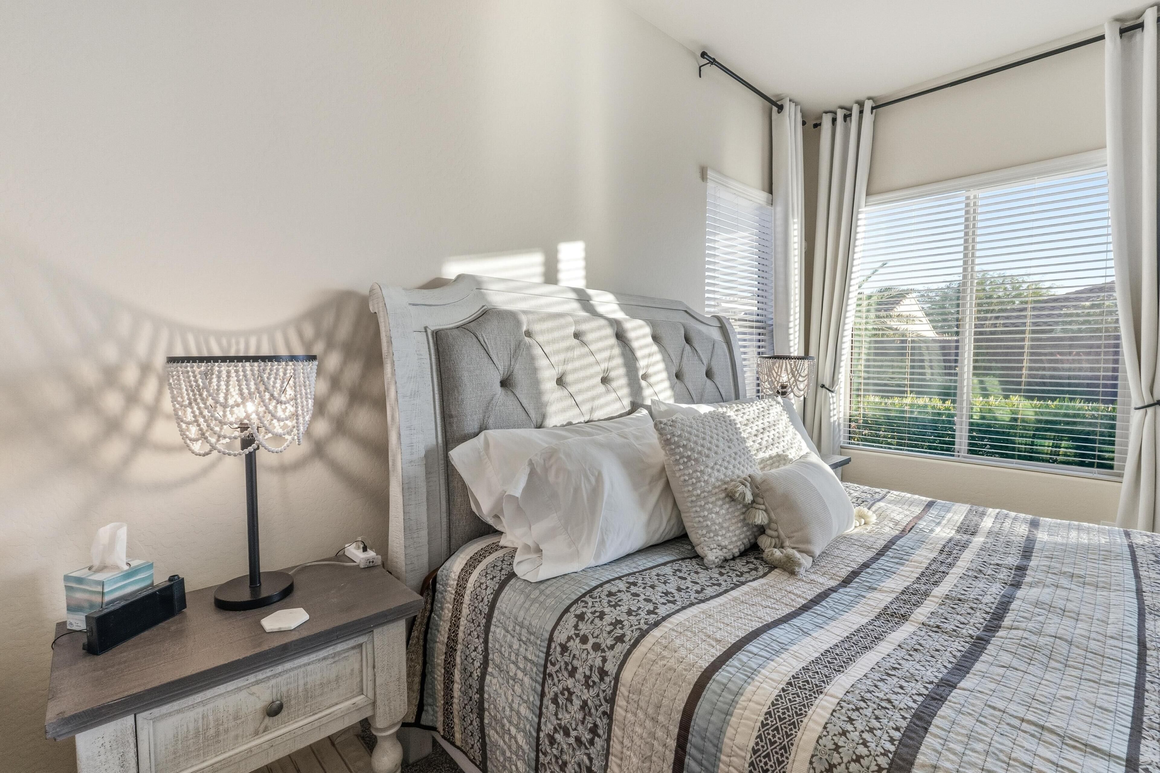 Une chambre à coucher avec un lit, une table de chevet, une lampe et une fenêtre avec des stores.