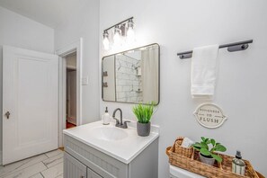 Un bany amb un lavabo blanc, un mirall, un suport per a tovalloles, una cistella amb productes de tocador i un cartell que diu "REMEMBER TO FLUSH".