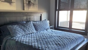 A bed with a quilted bedspread and two pillows, a wooden headboard, and a window with a view of a white fence.