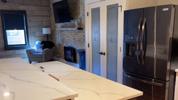 A kitchen with a marble countertop, a black refrigerator, and a brick wall.