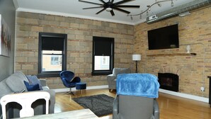 A living room with a brick wall, a fireplace, a ceiling fan, and a large window.