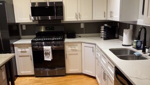 A modern kitchen with stainless steel appliances, white cabinetry, and a marble countertop.