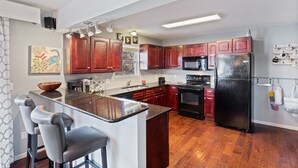 Een moderne keuken met donkere houtkasten, een zwarte koelkast en een granieten aanrechtblad met barstoelen.