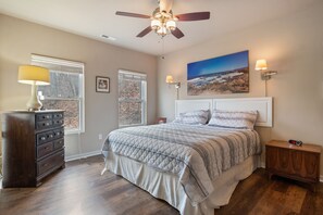 A bedroom with a bed, dresser, nightstand, ceiling fan, and artwork on the wall.