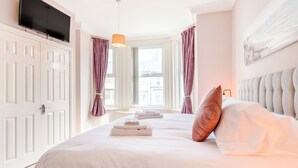 Hotellihuone, jossa on sänky, seinälle asennettu taulutelevisio, ikkuna, jossa on verhot, ja seinällä oleva taulu.