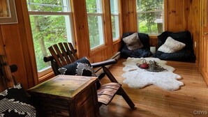 Ein gemütliches Blockhaus-Interieur mit Holzwänden, großen Fenstern, einem Holztisch, Stühlen, einem Fellteppich und einem Kamin.