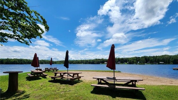 Ein Picknickplatz am Seeufer mit Picknicktischen und Sonnenschirmen, umgeben von Wiesen und Seeblick.