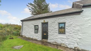 A white stone house with a black door, two windows, and a small garden. - A tiny, traditional cottage tucked away on the Ross of Mull, close to the sea. (Isle of Mull)