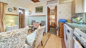 A cozy room with a bed, a table with chairs, a small kitchen area with a washing machine, and a door leading to another room. - A tiny, traditional cottage tucked away on the Ross of Mull, close to the sea. (Isle of Mull)