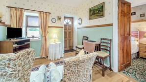 A cozy room with a television, a small table with a lamp, floral-patterned chairs, and a wooden door. - A tiny, traditional cottage tucked away on the Ross of Mull, close to the sea. (Isle of Mull)