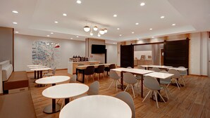 Un espace repas moderne avec des tables et des chaises rondes, un coin bar équipé d’un téléviseur et un grand tableau abstrait accroché au mur.