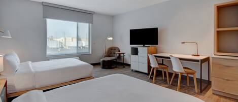 A hotel room with two beds, a desk, a TV, and a large window.