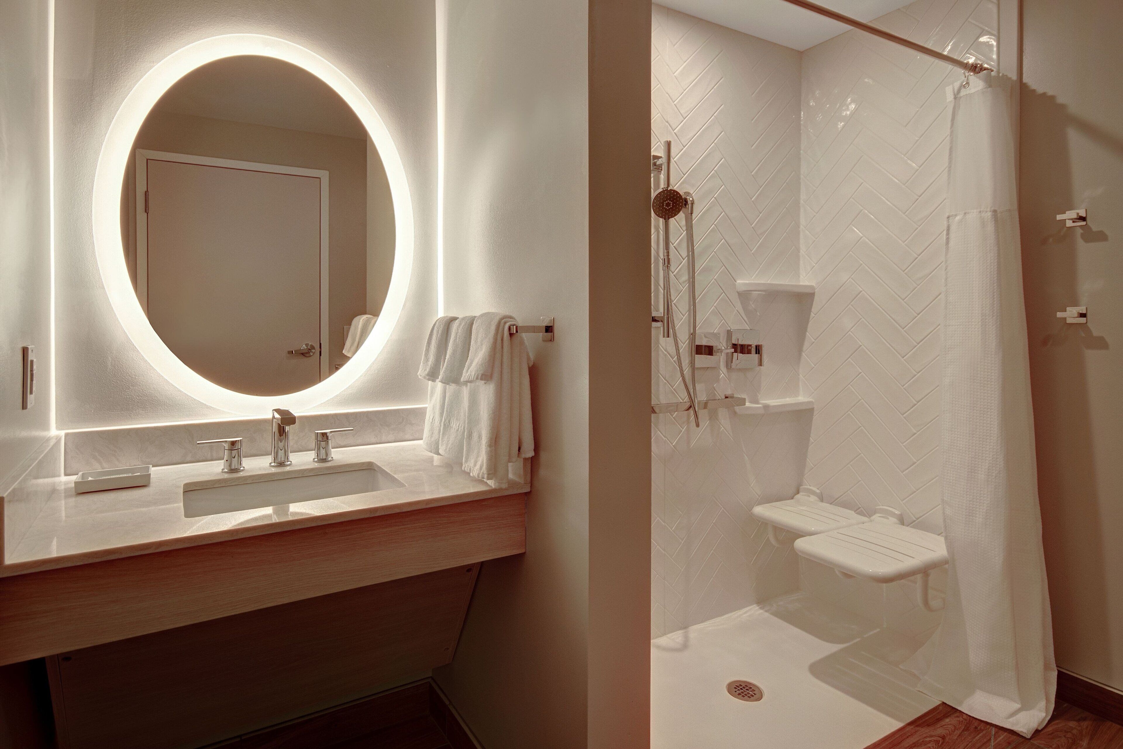 A bathroom with a round mirror, a sink, and a shower area with a herringbone-patterned wall.