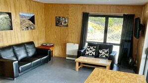 Una sala de estar moderna con piso de madera, un sofá de cuero negro, una mesa de centro de madera y un ventanal con cortinas.
