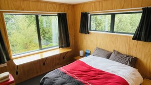 Un dormitorio con una cama, dos ventanas, una mesita de noche y un tocador.