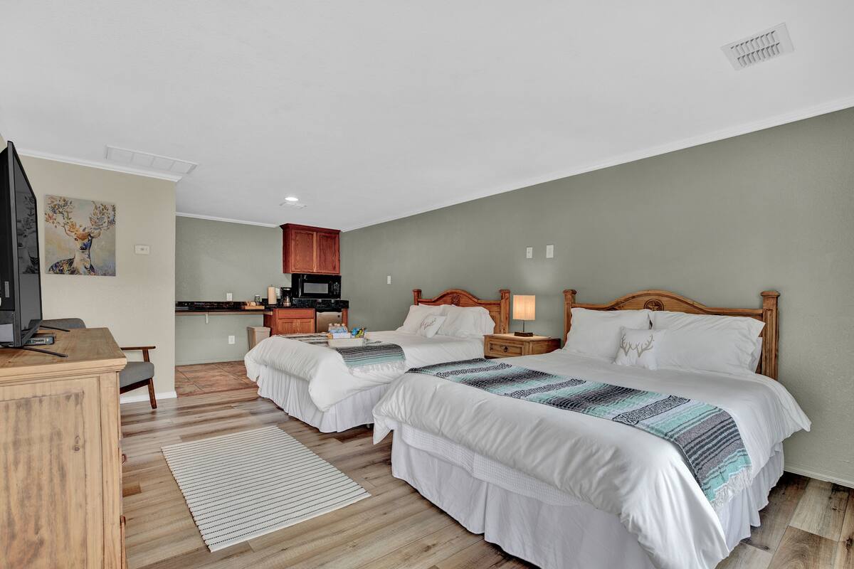 A hotel room with two beds, a desk, a television, and a kitchenette.