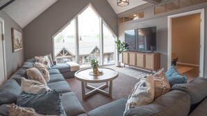 Un salon spacieux avec un grand canapé d’angle, une table basse ronde et un téléviseur posé sur un meuble en bois.