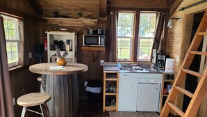 Une cuisine compacte aux murs en bois, avec une table ronde, un tabouret, un réfrigérateur et un four à micro-ondes.