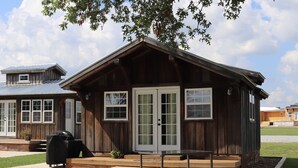 Une cabane en bois avec une véranda, un barbecue et une petite table.