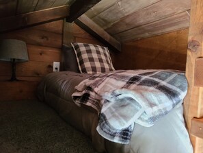 A cozy bedroom with a bed, a checkered pillow, a lamp, and a wooden ceiling. - Romantic Country Cabin at Lakeview by Sue  (Appleton City)