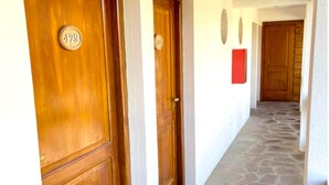 A hallway with wooden doors numbered 129 and 130, leading to a room with a red accent wall and a stone floor. - Loft Catedral by Base 41 (San Carlos de Bariloche)