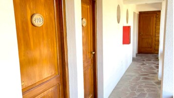 A hallway with wooden doors numbered 129 and 130, leading to a room with a red accent wall and a stone floor.