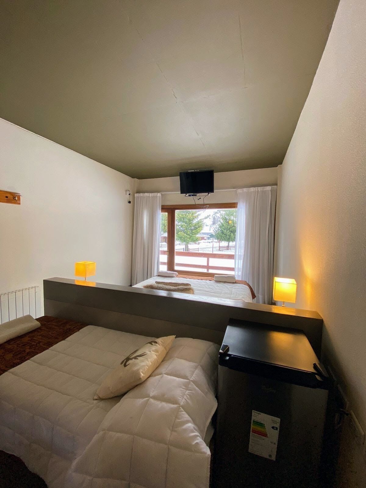Habitación de hotel con cama, escritorio, televisor montado en la pared y ventana con cortinas.