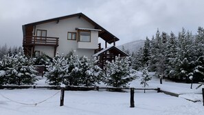 Un chalet à deux étages doté d’un balcon, entouré d’arbres couverts de neige.