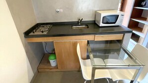 A compact kitchen with a gas stove, a microwave, a sink, and a glass table with a chair. - Loft Catedral by Base 41 (San Carlos de Bariloche)