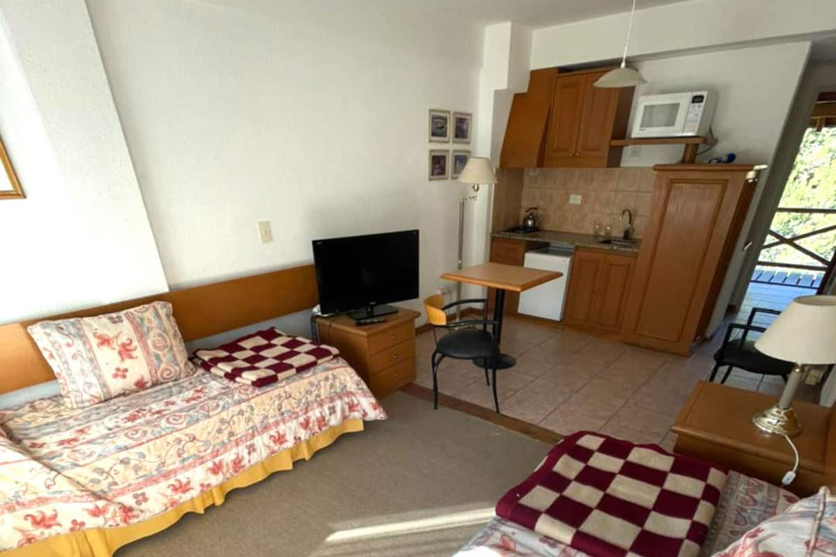 A hotel room with two beds, a desk, a television, a microwave, and a kitchenette.