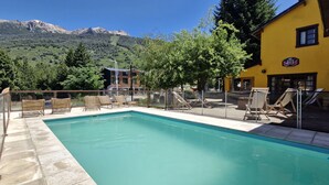 A pool area with lounge chairs and a yellow building in the background. - Loft Catedral by Base 41 (San Carlos de Bariloche)