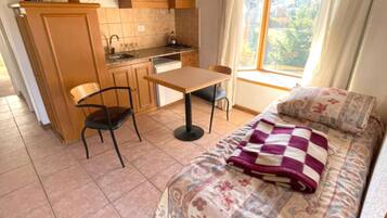 Una habitación compacta con kitchenette, comedor y cama con una colcha estampada.