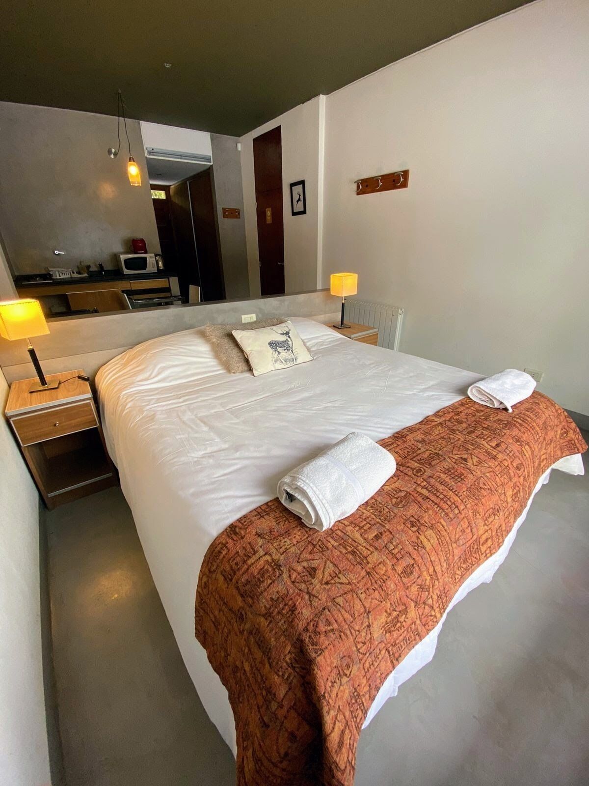 Habitació d'hotel amb un llit gran, dues làmpades de nit, un mirall, un escriptori amb microones i una manta vermella amb dibuixos.