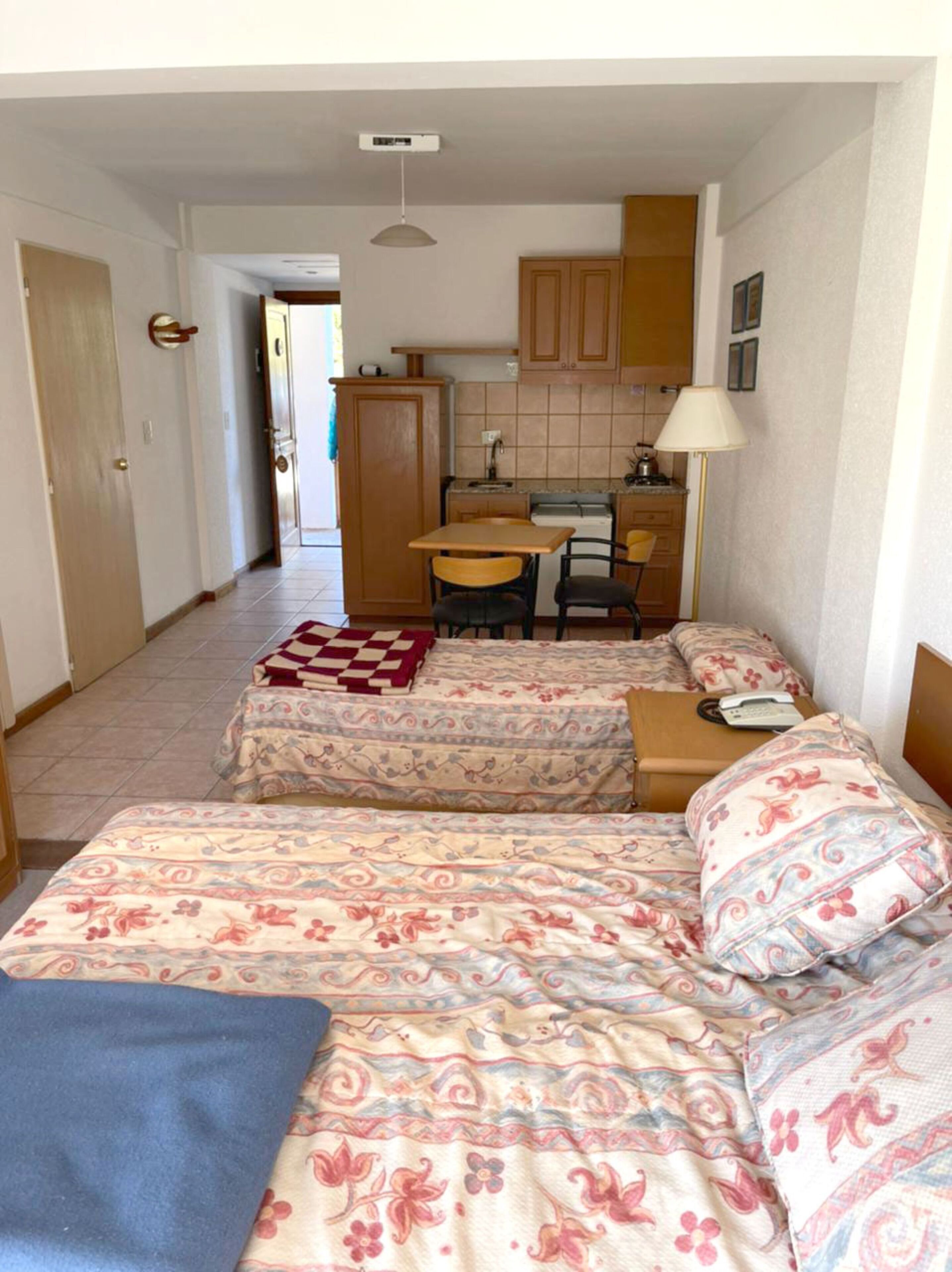A compact room with two beds, a small kitchenette, and a dining area.