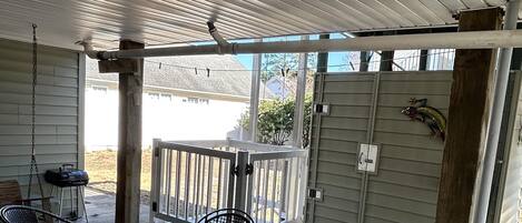A covered patio with a table and chairs, a grill, and a wooden fence.
