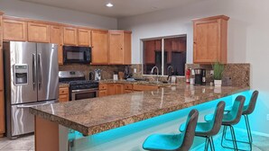 Eine moderne Küche mit Granit-Arbeitsplatten, Edelstahlgeräten, Holzschränken und einer Bar mit Barhocker.