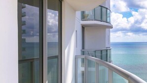 A balcony with a glass railing overlooking a calm sea and a partly cloudy sky. - Private Oceanfront Condominium with Beach Access and Resort Services (Sunny Isles Beach)