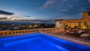 Una piscina en la azotea con vistas a un paisaje urbano al anochecer.