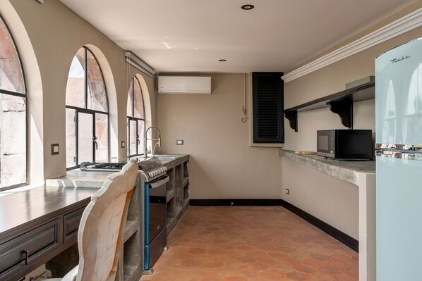A kitchen with a built-in oven, a microwave, and a refrigerator. There are three windows with arched tops, and a sink is visible.