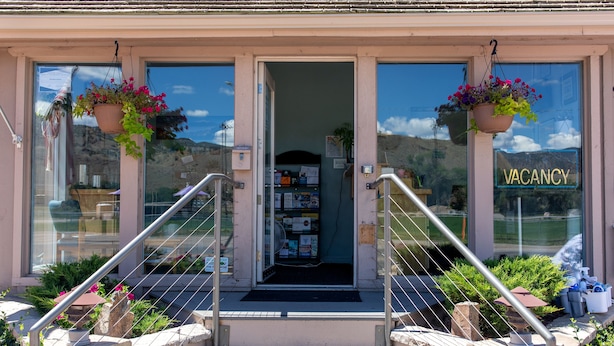 Entrada de hotel con un cartel de 'VACANCY', una escalera y cestas de flores colgantes.