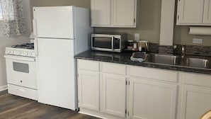 Una cocina con gabinetes blancos, estufa, refrigerador, microondas y pileta.