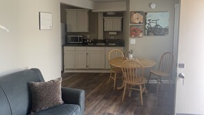 Un espacio habitable compacto con kitchenette, una zona de comedor con mesa y sillas, y un sofá con cojín.